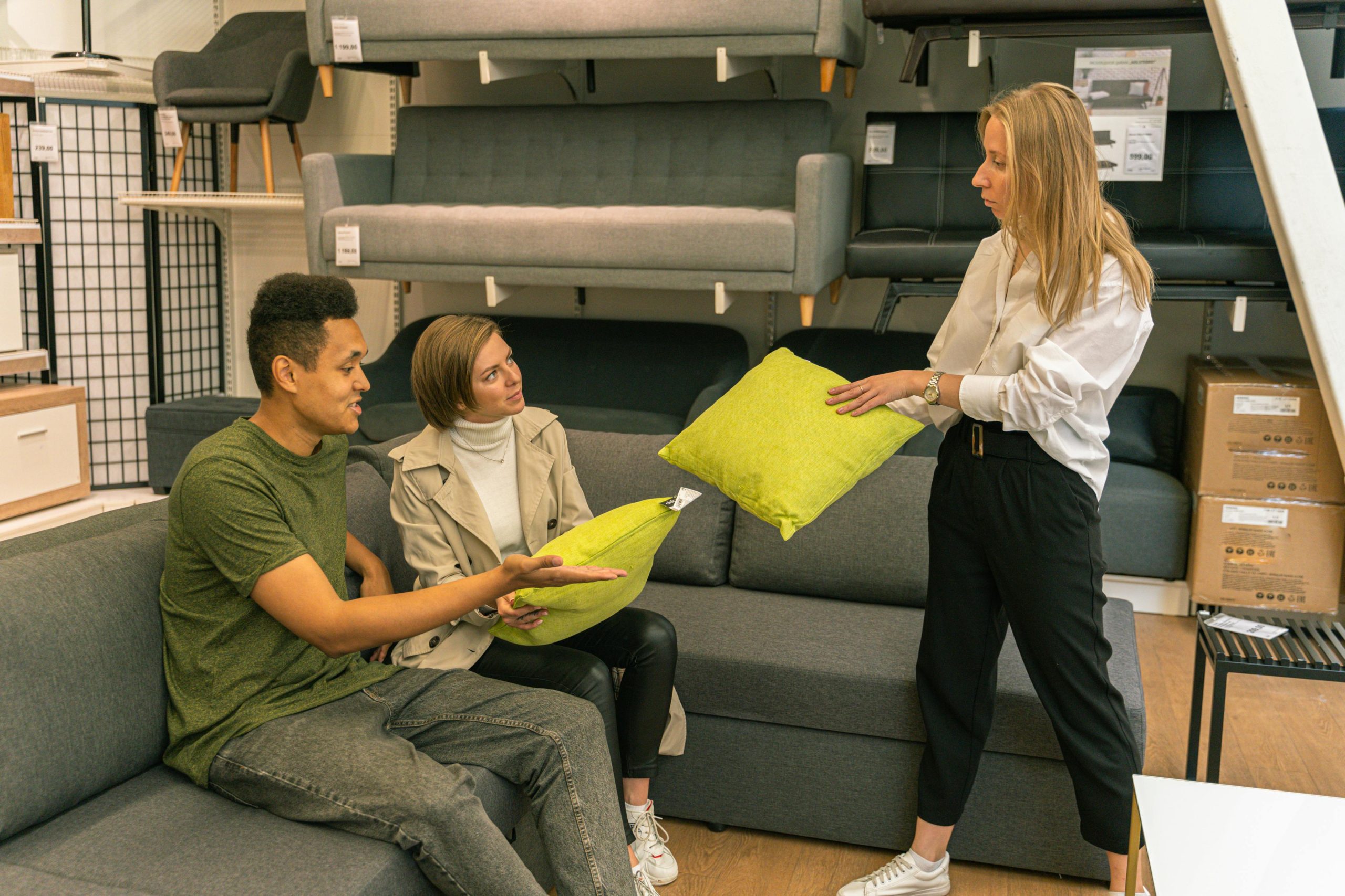 A couple selecting cushions with a salesperson in a furniture store, surrounded by sofas.