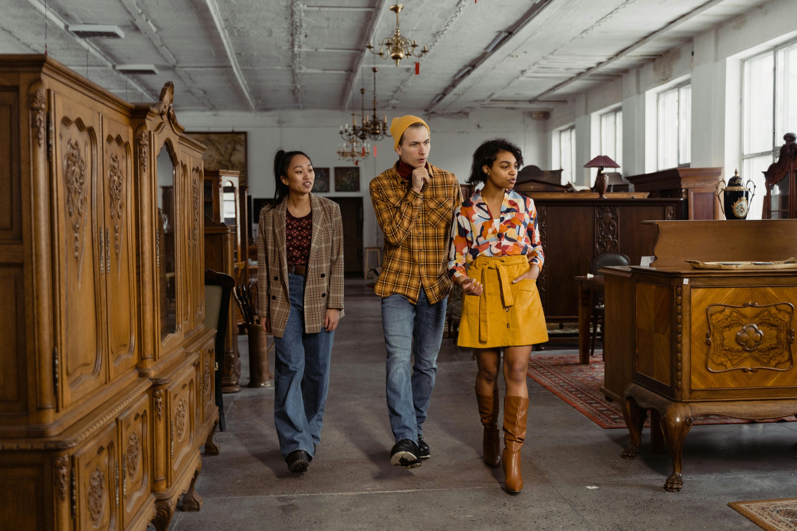 Fashionable friends browsing an antique store showcasing vintage wooden furniture indoors.