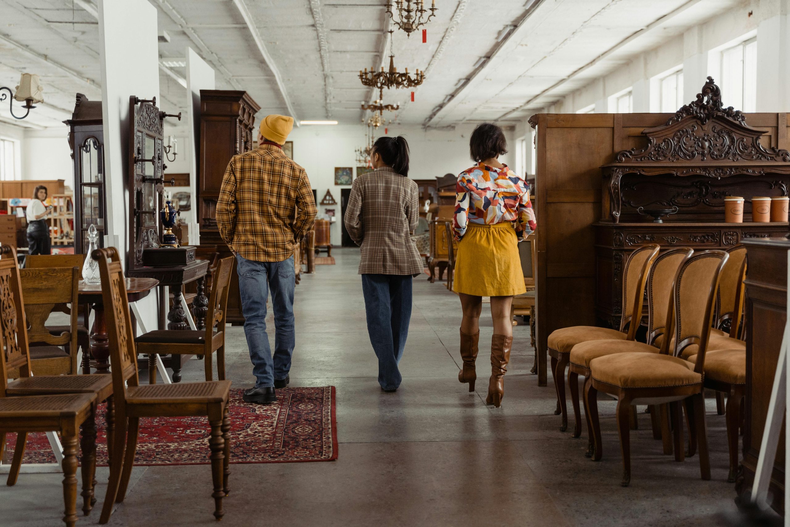 People walking through an antique furniture store, surrounded by vintage chairs and decor.