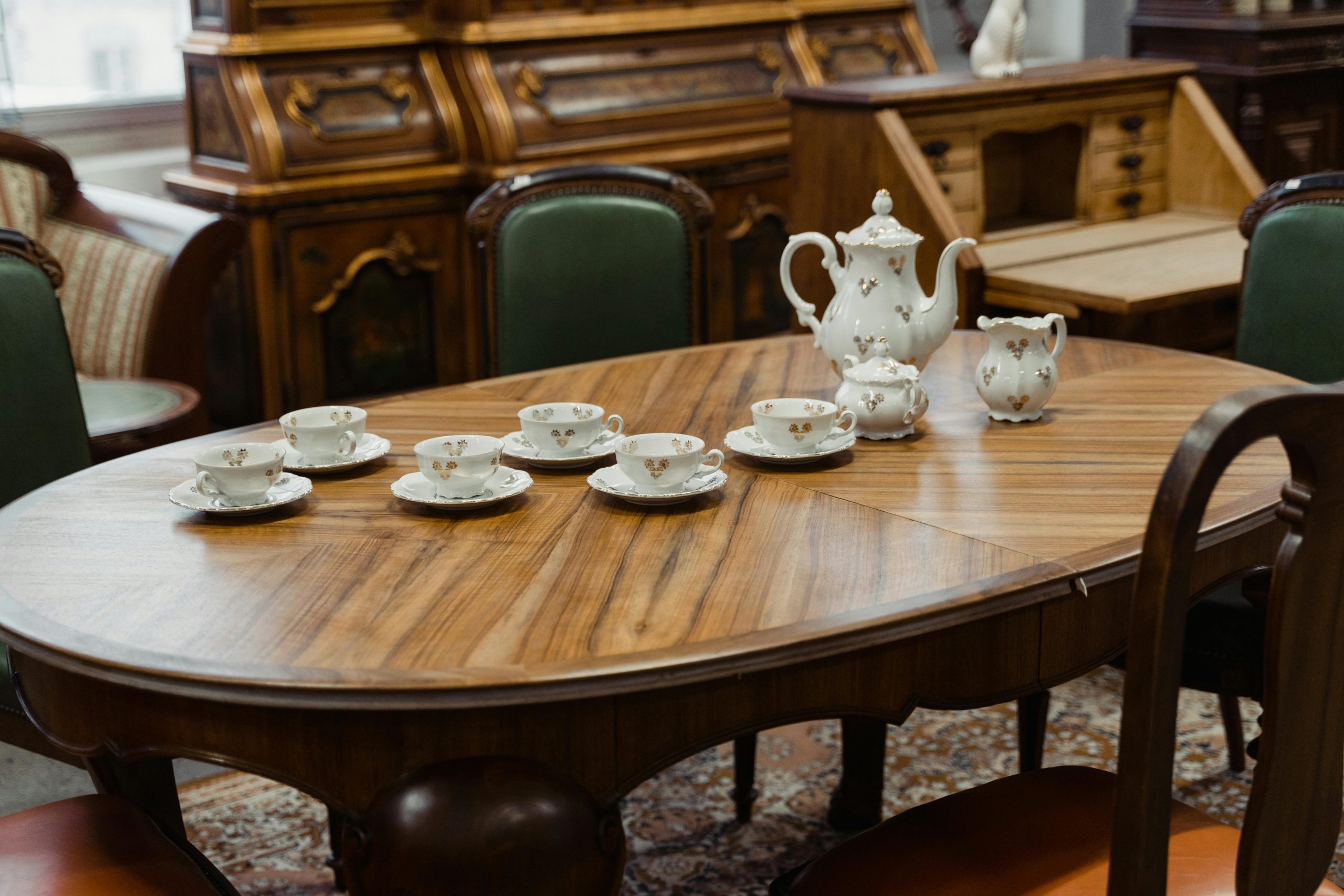 Vintage dining table featuring an elegant porcelain tea set in an antique shop setting.